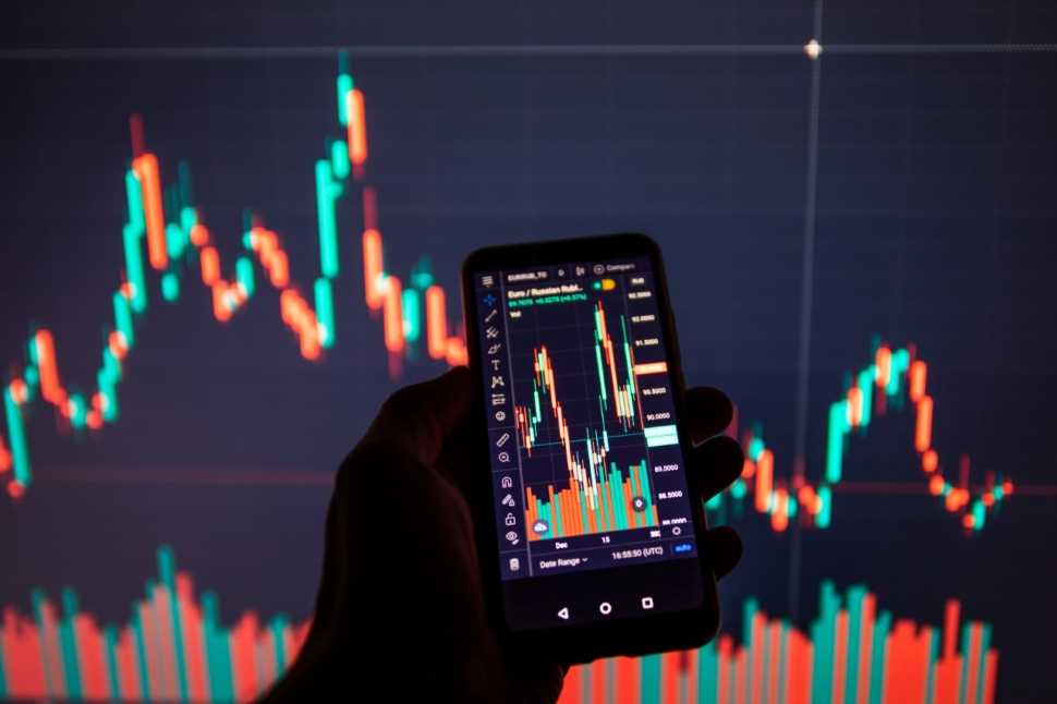 Pessoa segurando celular com gráficos- Remete variação do mercado financeiro