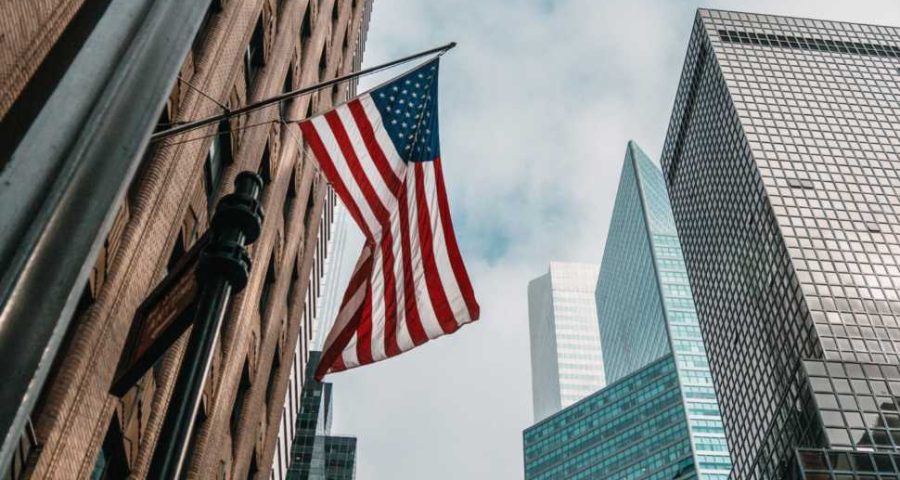 a-bandeira-dos-eua-ou-estados-unidos-da-america-em-um-mastro-de-bandeira-perto-de-arranha-ceus-sob-um-ceu-nublado